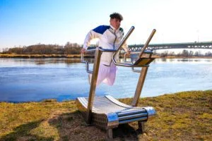 a young man with a serious face is exercising on an outdoor treadmill by the water, second image