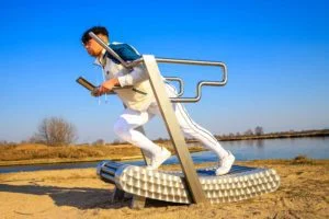a young man with a serious face is exercising on an outdoor treadmill by the water